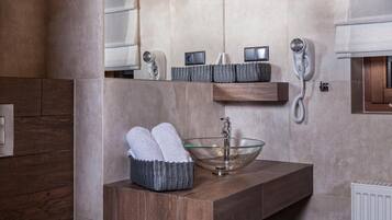A modern bathroom with a wooden vanity, a glass bowl sink, and two pendant lights.
