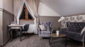 A cozy room with a grey armchair, a sofa, a round coffee table, a small table with bottles, and a window with curtains. - Willa w Dolinie (Tarnow)