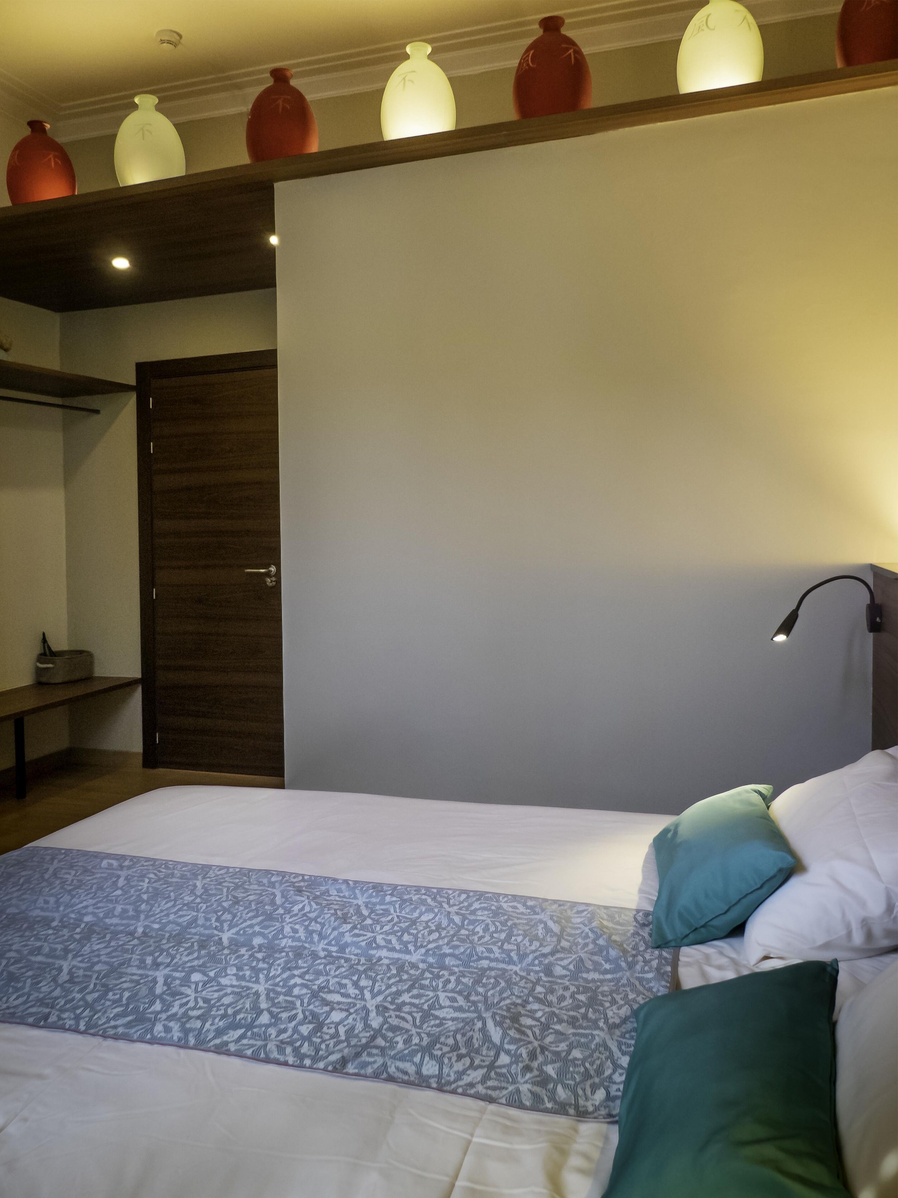 Ein Schlafzimmer mit einem Bett, einem Nachttisch, einer Lampe und dekorativen Vasen an der Wand.