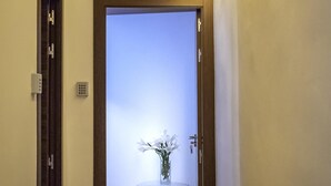 A hallway with a door leading to a room with a view. There is a small table with a vase of flowers in the room. - Pensión Ciudadela (Barcelona)