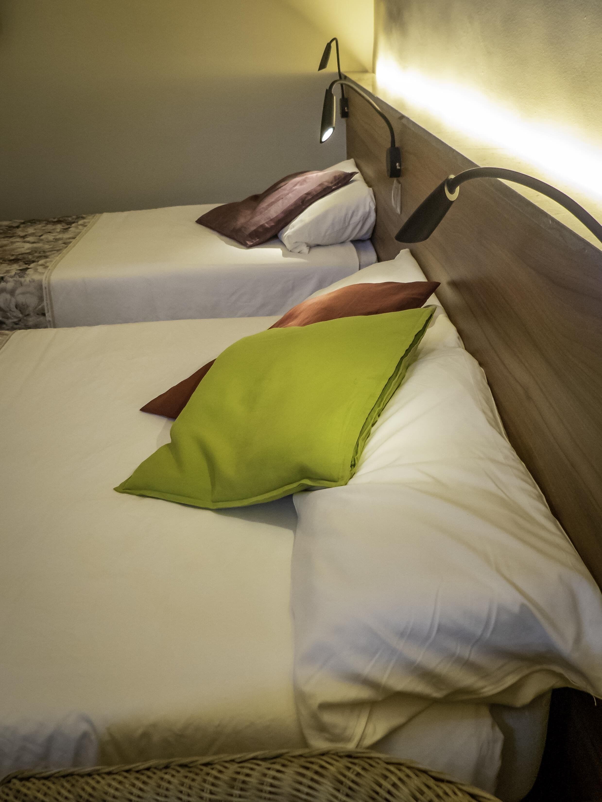 Two single beds with wooden headboards, white bedding, and a green pillow.