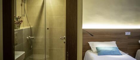 A compact hotel room with a shower, toilet, and a bed with a pillow.