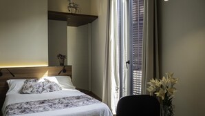 A bedroom with a bed, a nightstand, a vase with flowers, and a chair. - Pensión Ciudadela (Barcelona)
