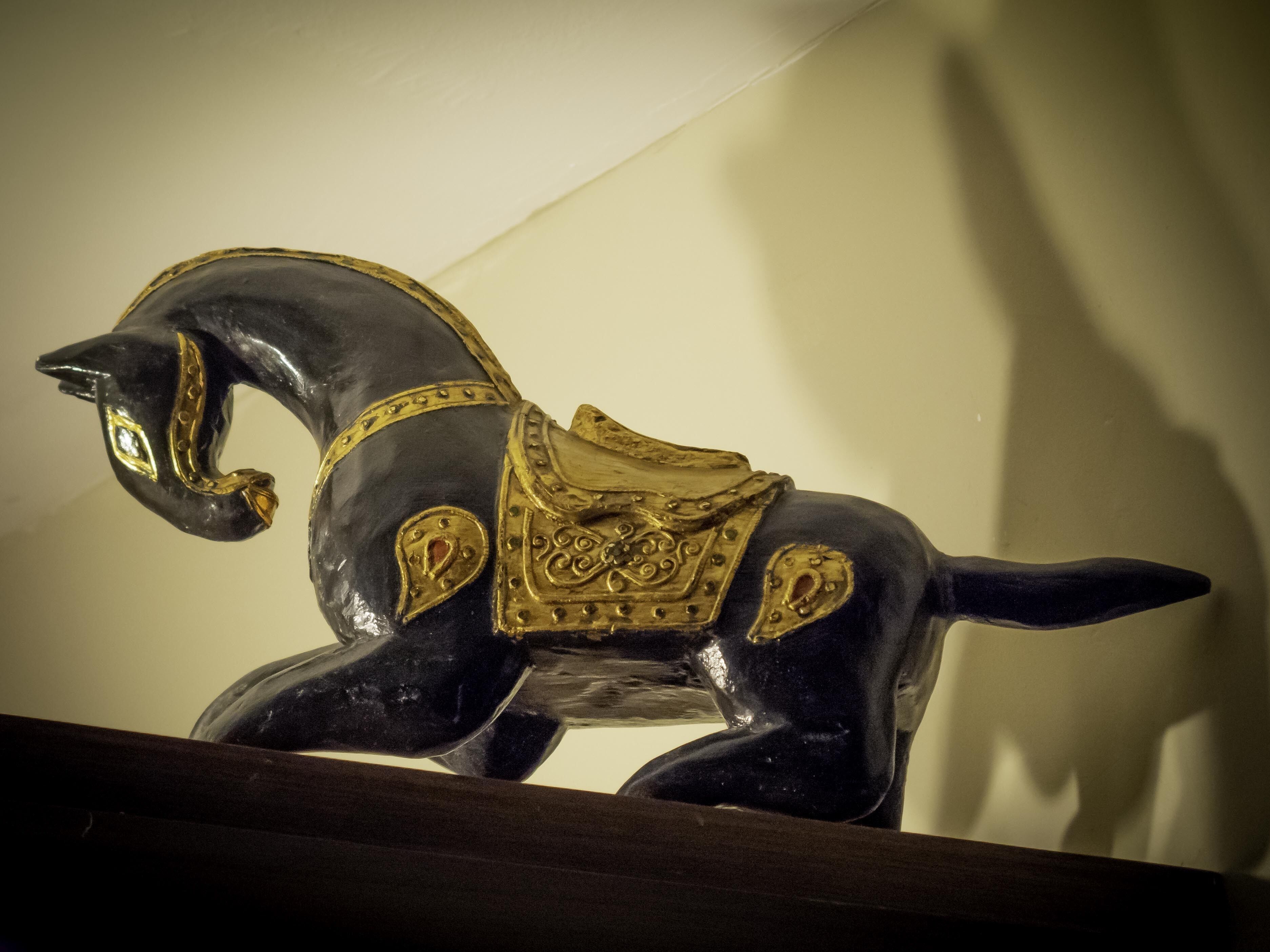 Una escultura decorativa de un caballo en color negro y dorado sobre una estantería.