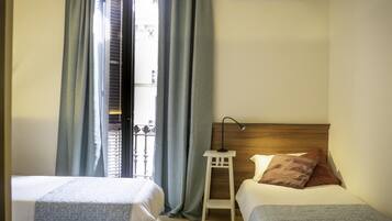Een hotelkamer met twee bedden, een nachtkastje, een lamp en uitzicht op het balkon.
