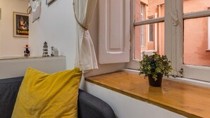 A cozy room with a wooden window sill, a potted plant, and a yellow pillow on a grey sofa. - Gladiator's House (Rome)