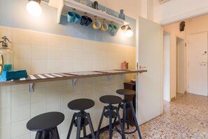 A kitchen with a wooden countertop, hanging mugs, and stools. - Residenza Novecento (Verona)