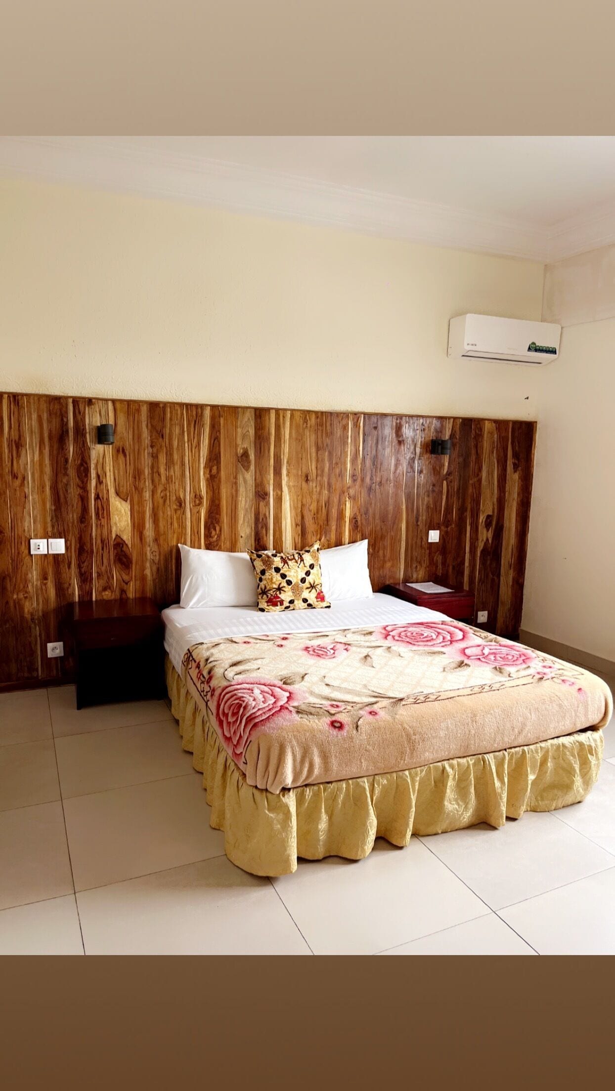 A bedroom with a wooden headboard, a bed with a floral bedspread, and a white air conditioning unit on the wall.