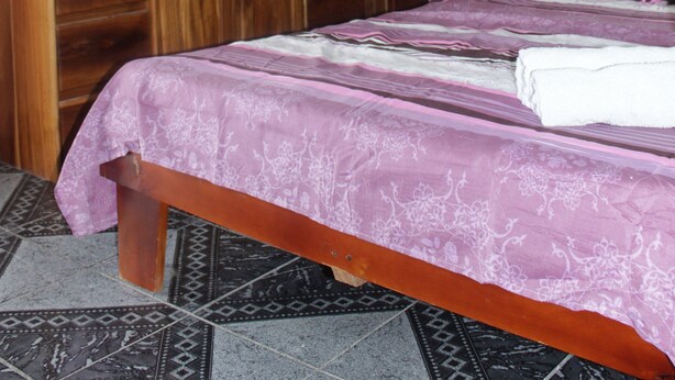 Un dormitorio con estructura de cama de madera, una ventana con cortinas blancas y un aire acondicionado instalado en la pared.