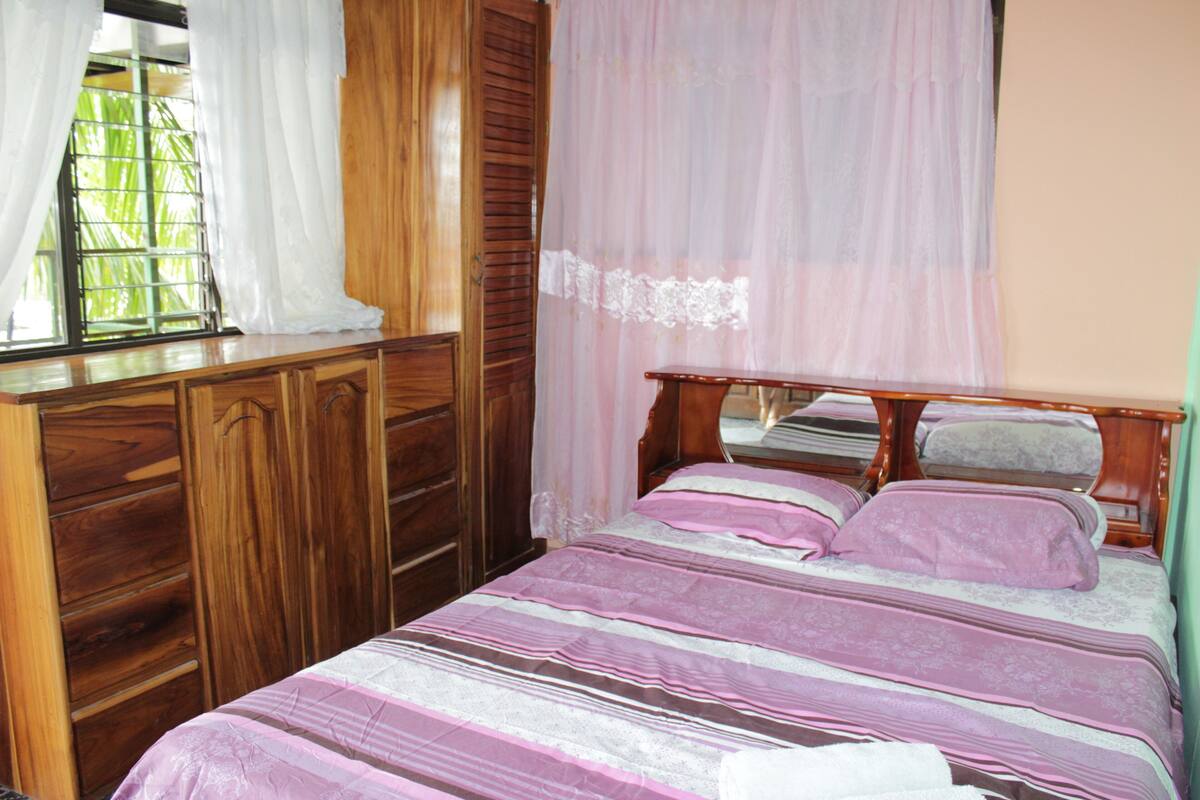 A bedroom with a wooden bed frame, a window with curtains, and a wooden wardrobe.