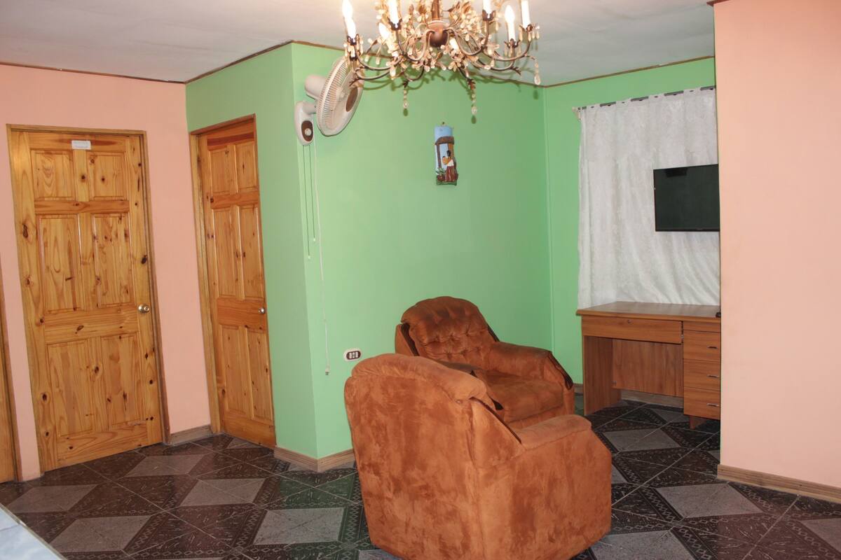 A room with a wooden door, a fan, a chair, a desk, and a chandelier.
