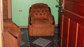 Ein Zimmer mit einem braunen Sessel, einer Holztür und einem Wandventilator.