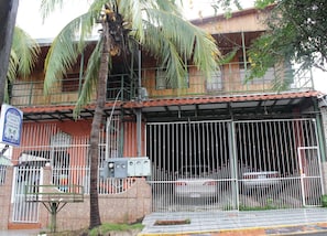 Un edificio con entrada protegida por una verja, un cartel y un coche estacionado.