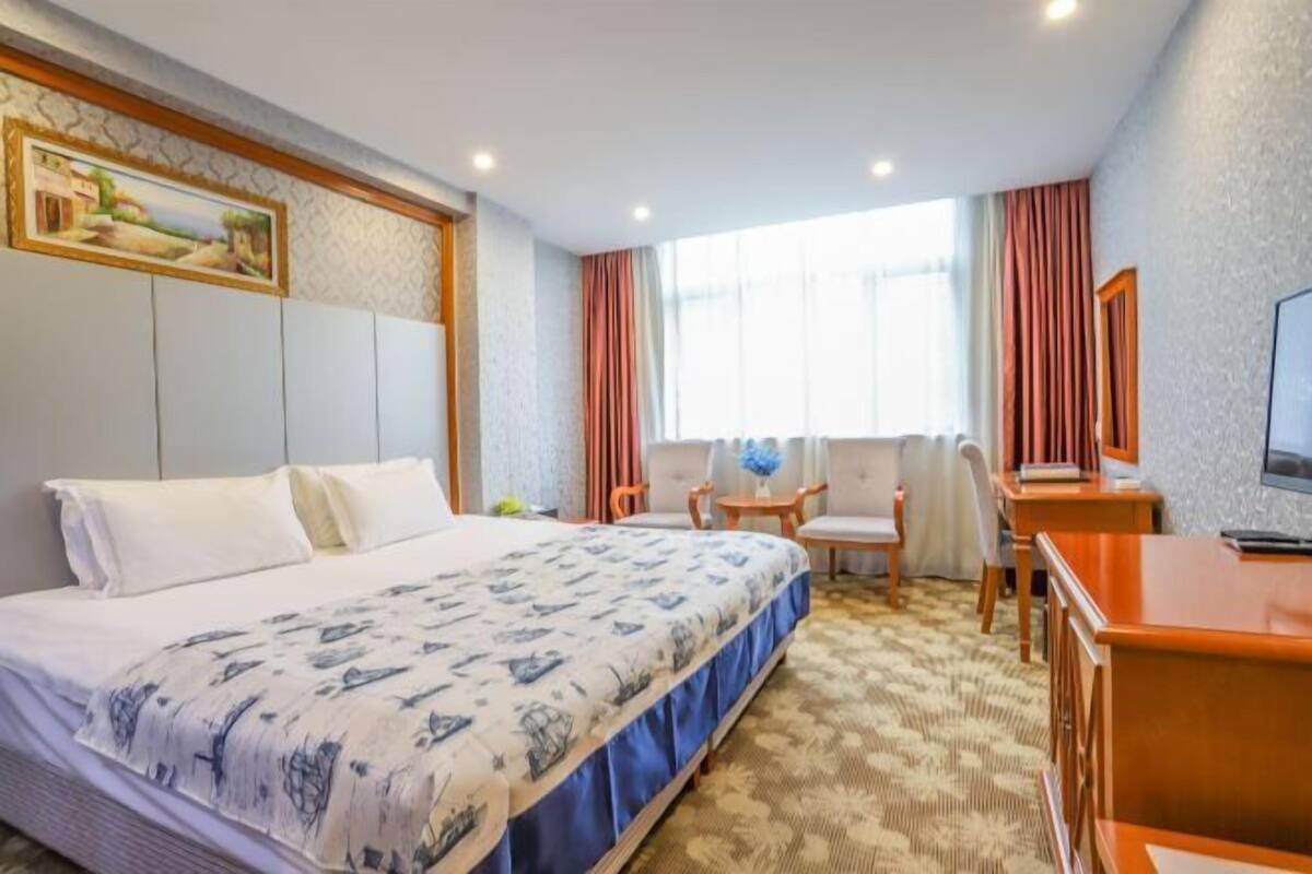 A hotel room with a bed, a desk, a chair, a TV, and a window with curtains.
