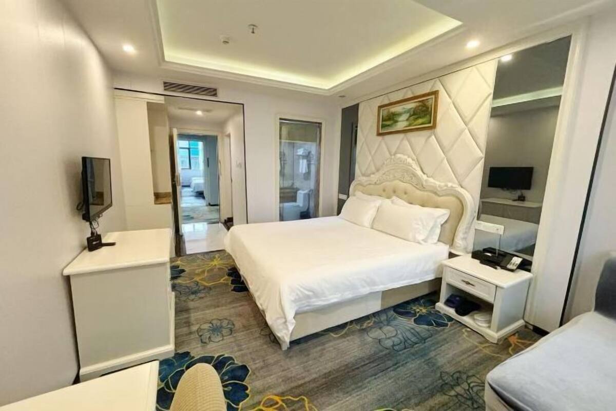 A hotel room with a large bed, a bedside table, a TV, and a wardrobe.