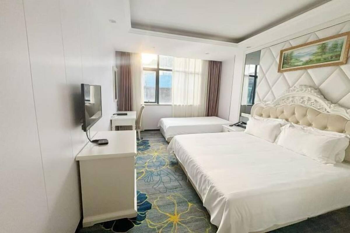 A hotel room with a large bed, a smaller bed, a desk with a TV, and a window with curtains.