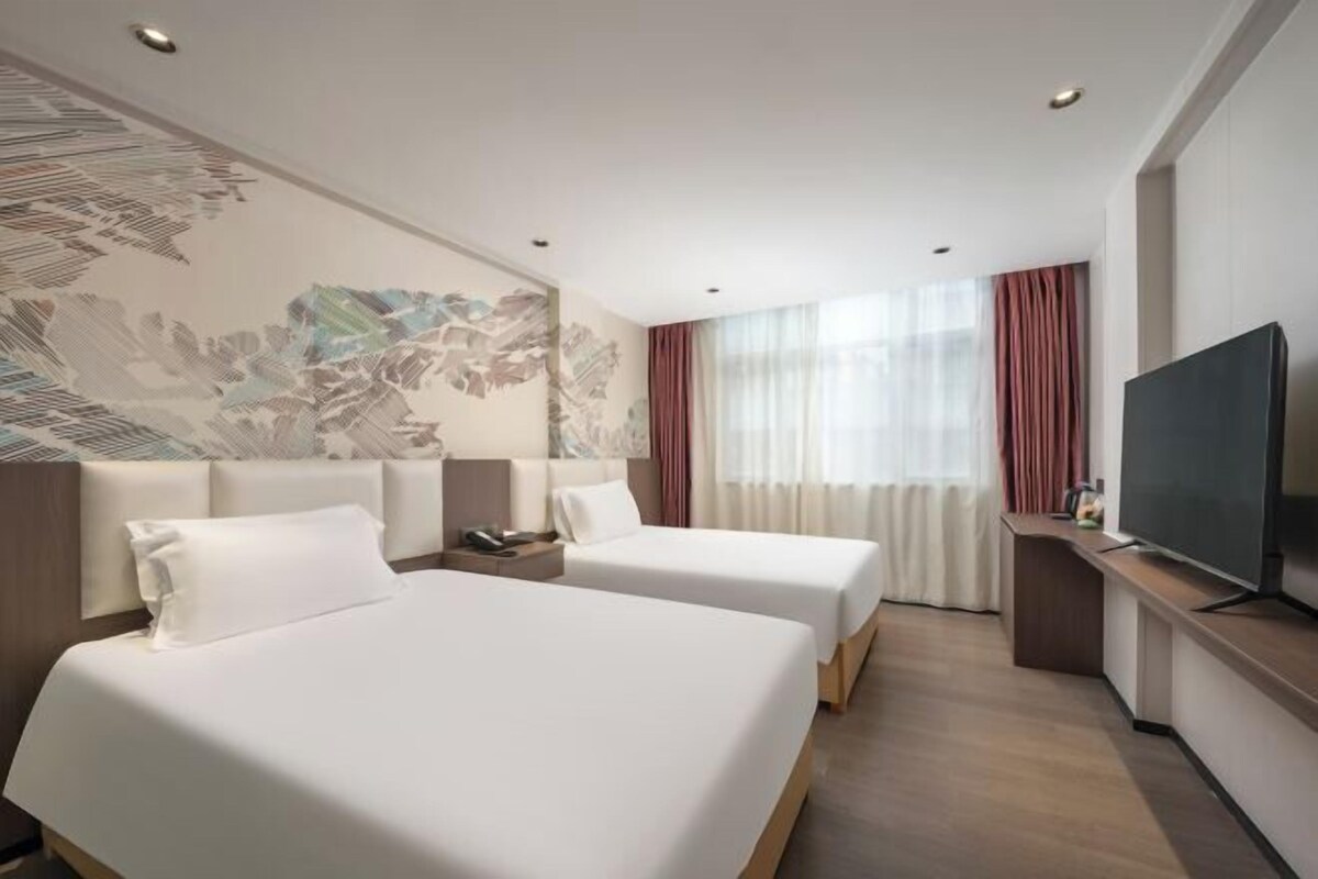 Ein Hotelzimmer mit zwei Betten, einem Fernseher und einem großen Fenster mit Vorhängen.