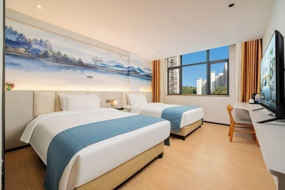 A hotel room with two beds, a desk, a television, and a large window with a city view.