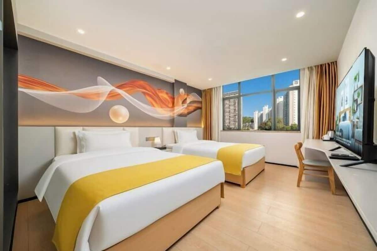 A hotel room with two beds, a desk, a television, and a large window with a city view.