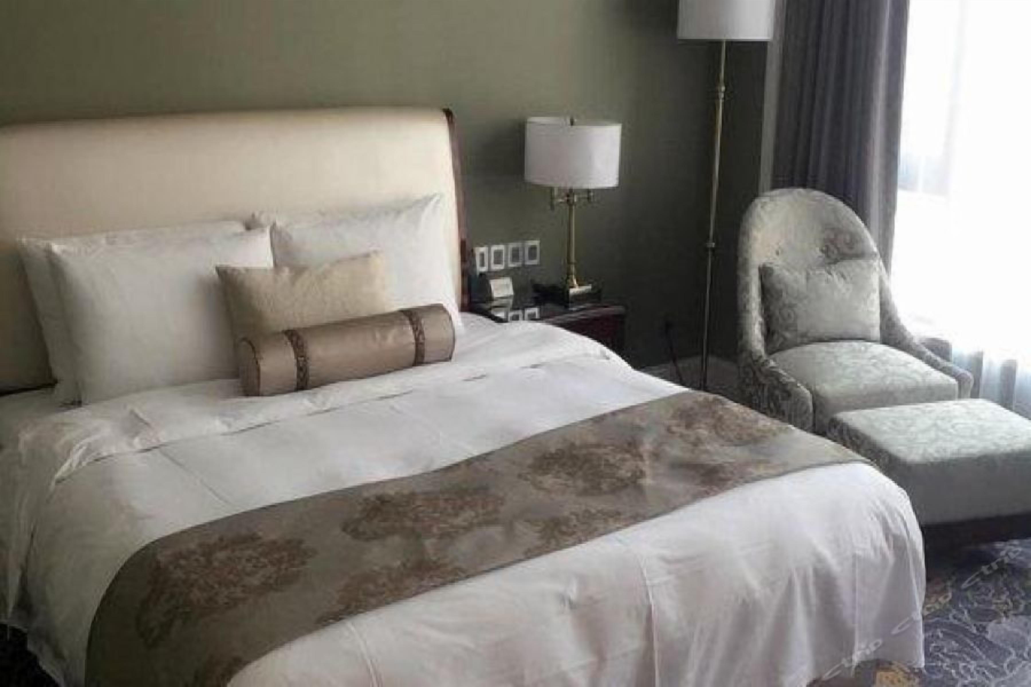 Una habitación de hotel con una cama grande, una silla, una mesita de noche y una lámpara.