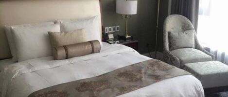Una habitación de hotel con una cama grande, una silla, una mesita de noche y una lámpara.