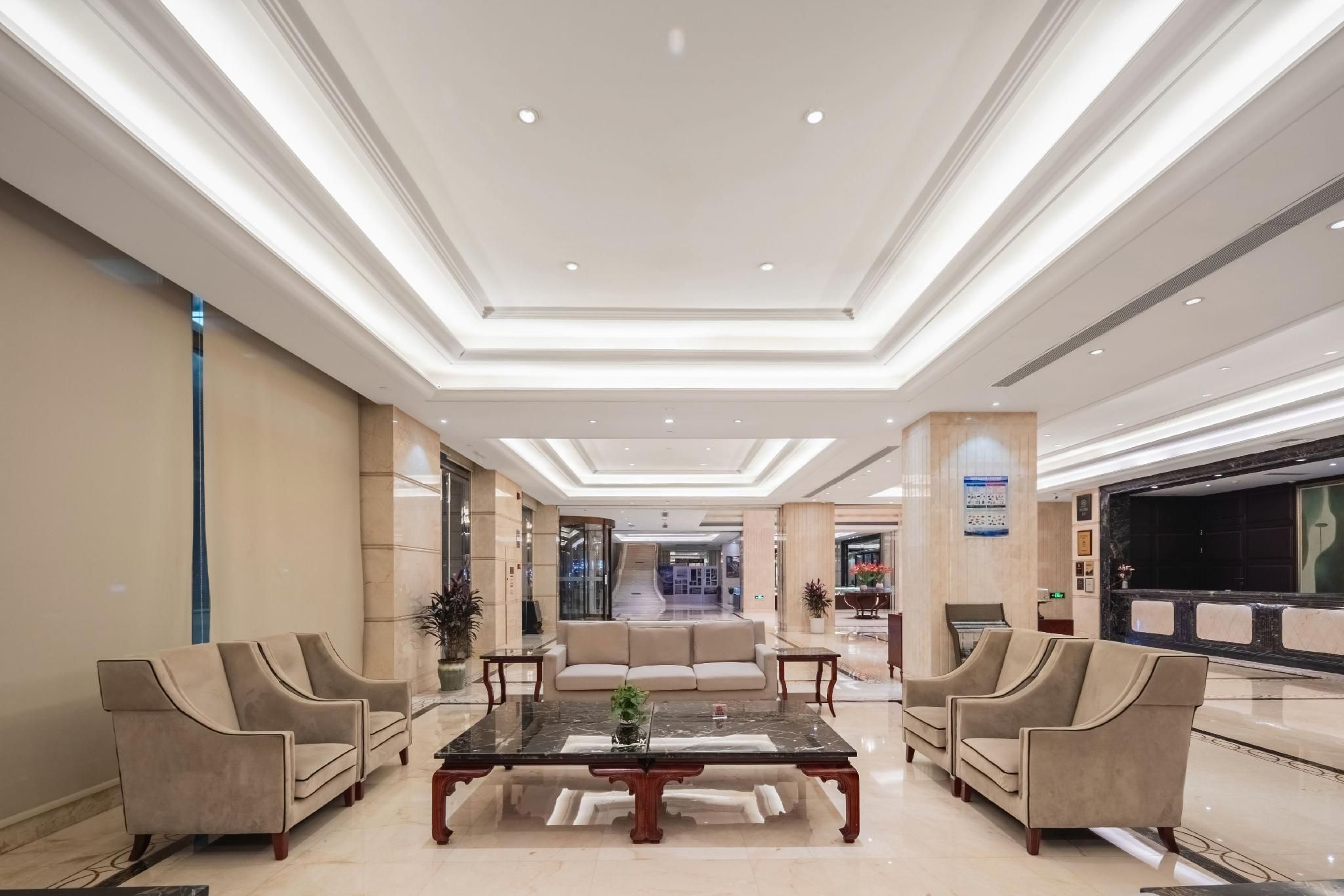 A spacious lobby with a central seating area, a reception desk, and a large television screen.