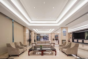 A spacious lobby with a central seating area, a reception desk, and a large television screen.