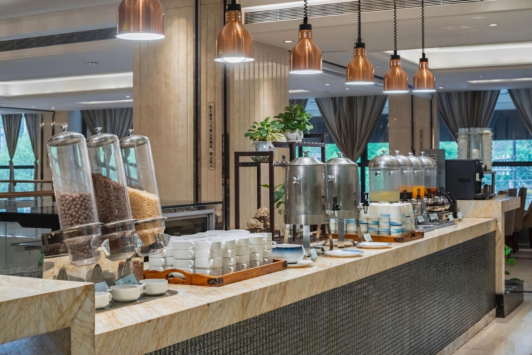 A buffet setup with various food containers, a coffee machine, and a counter with stacked cups.