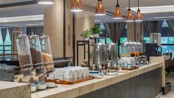 A buffet setup with various food containers, a coffee machine, and a counter with stacked cups.