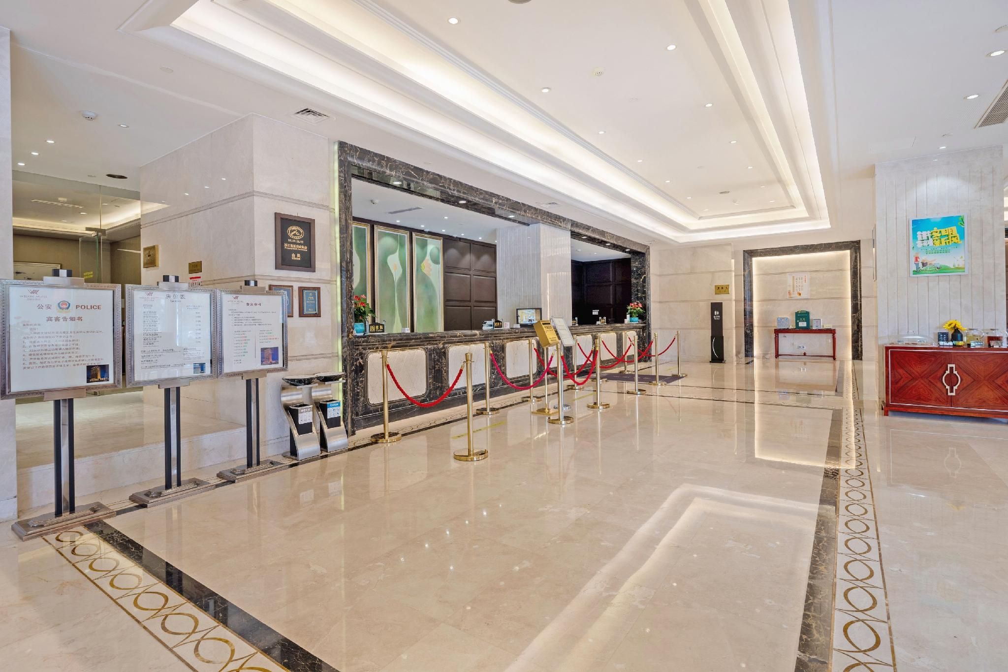 A hotel lobby with a reception desk, information boards, and a red carpeted area.