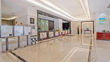 Vestíbulo de hotel con mostrador de recepción, tablones informativos y una zona alfombrada en rojo.