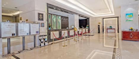 A hotel lobby with a reception desk, information boards, and a red carpeted area.