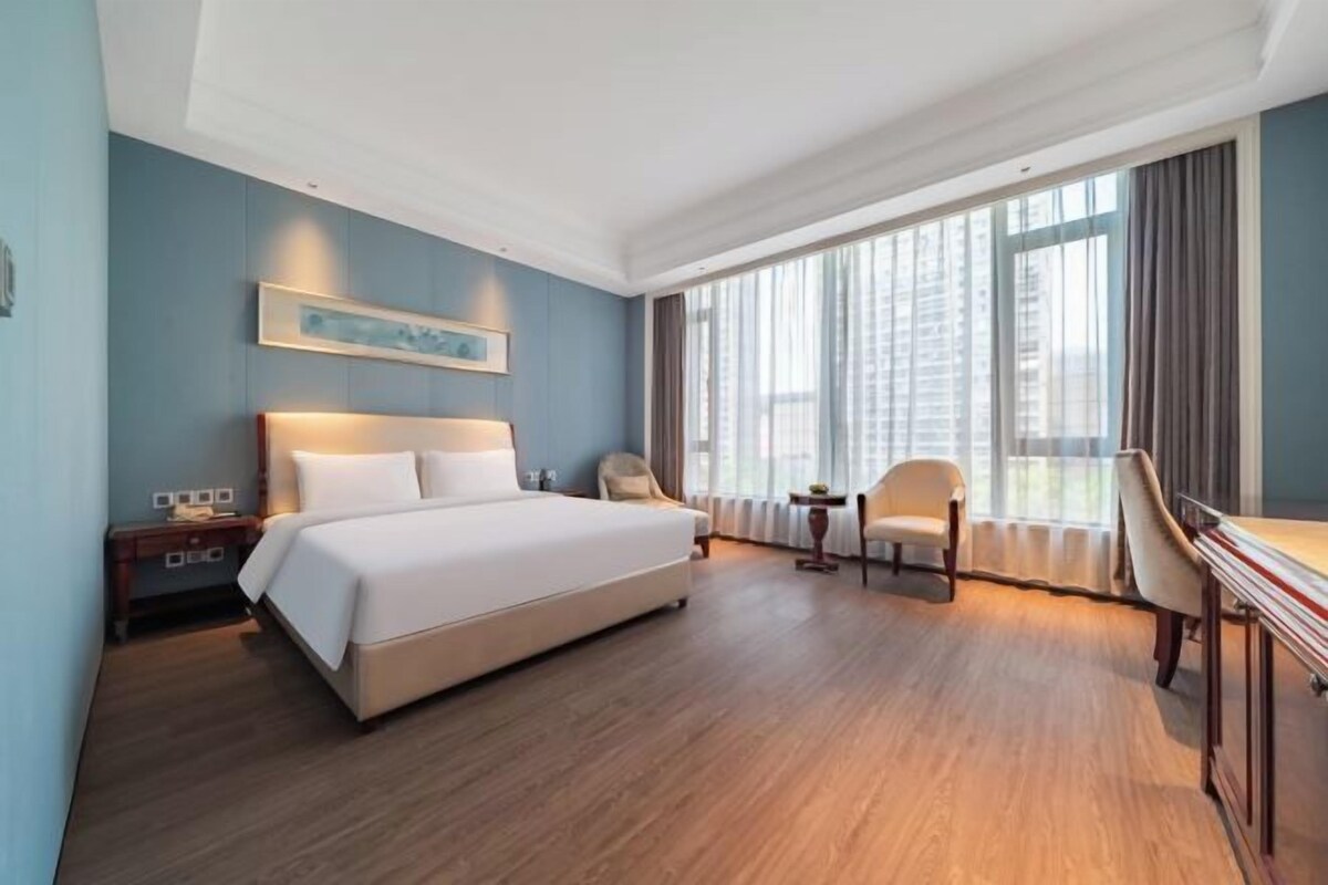 Una habitación de hotel con una cama grande, un escritorio, una silla y una ventana con cortinas.