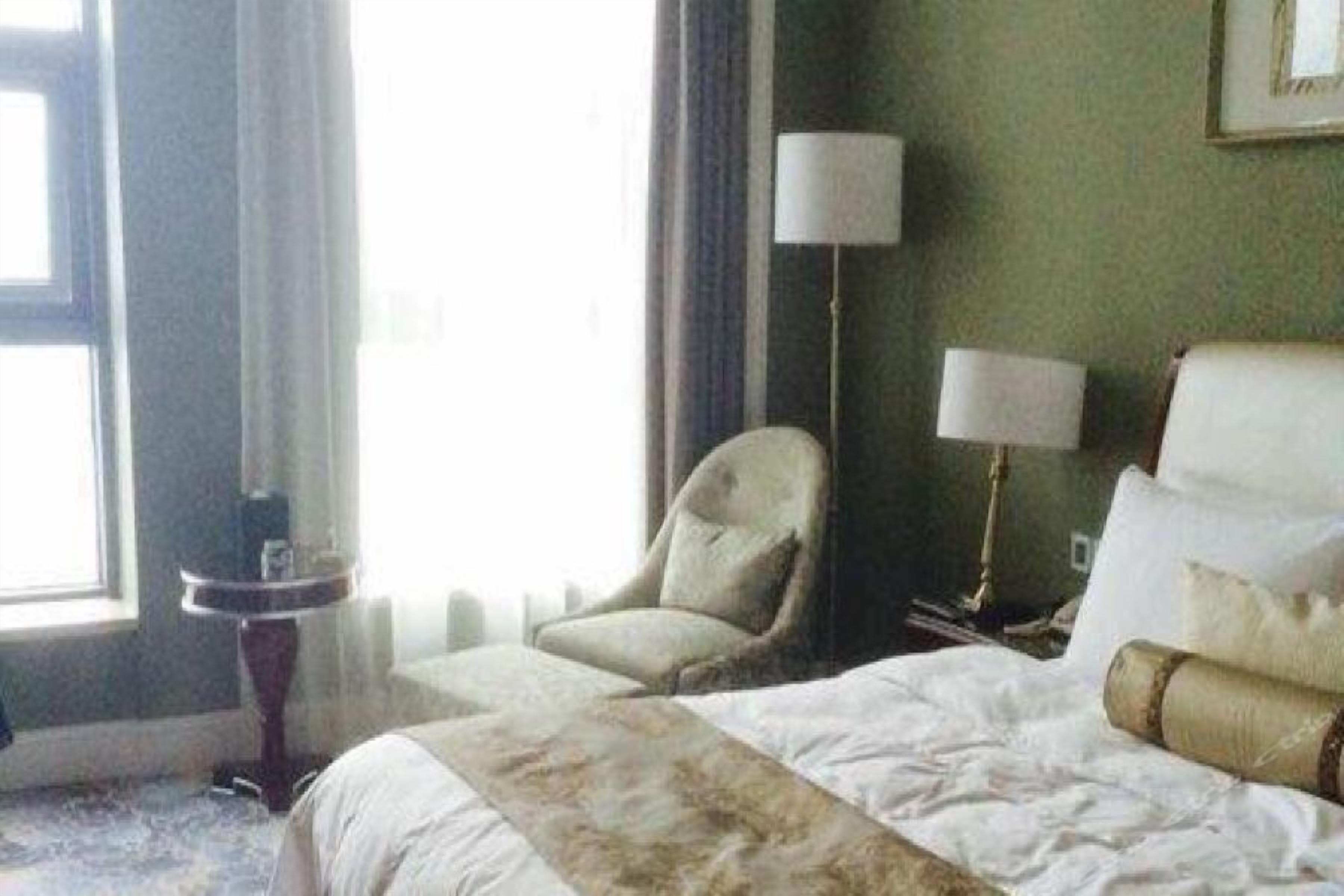 Una habitación de hotel con cama, una silla, una lámpara y una ventana.