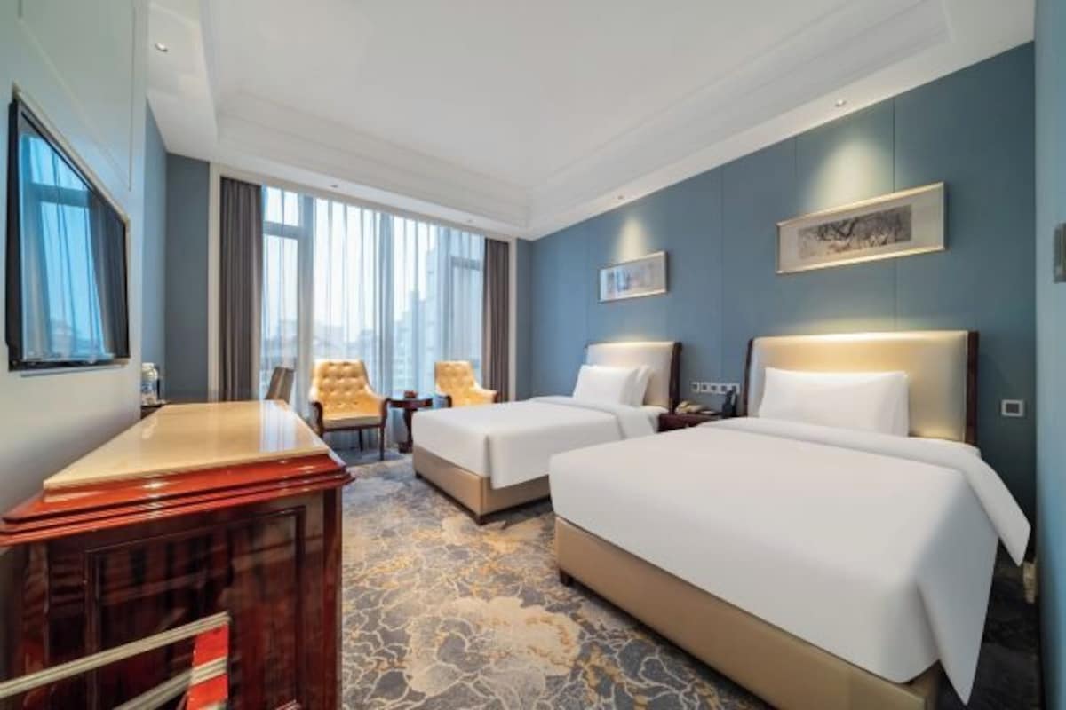 Une chambre d’hôtel avec deux lits, un bureau, une chaise et une grande fenêtre.