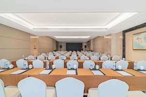Un salón de conferencias con filas de mesas, sillas y botellas de agua.