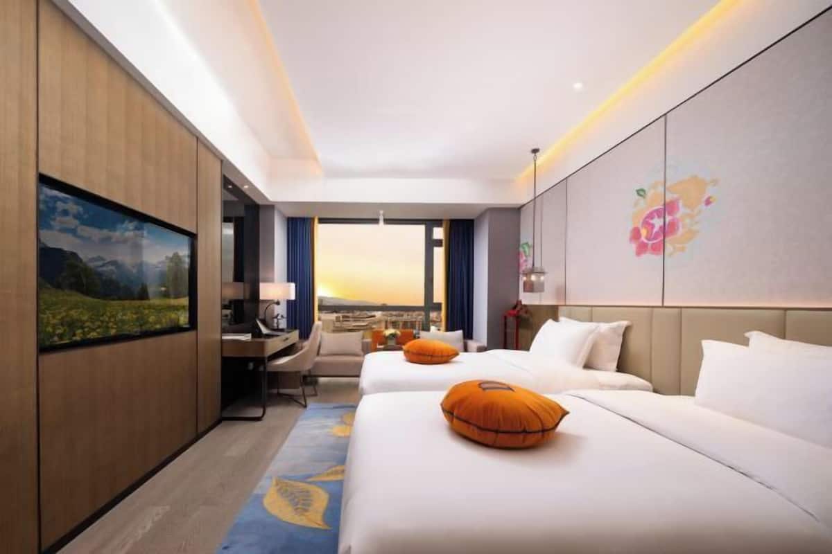 Une chambre d’hôtel avec deux lits, un bureau et une grande fenêtre donnant sur un beau paysage.