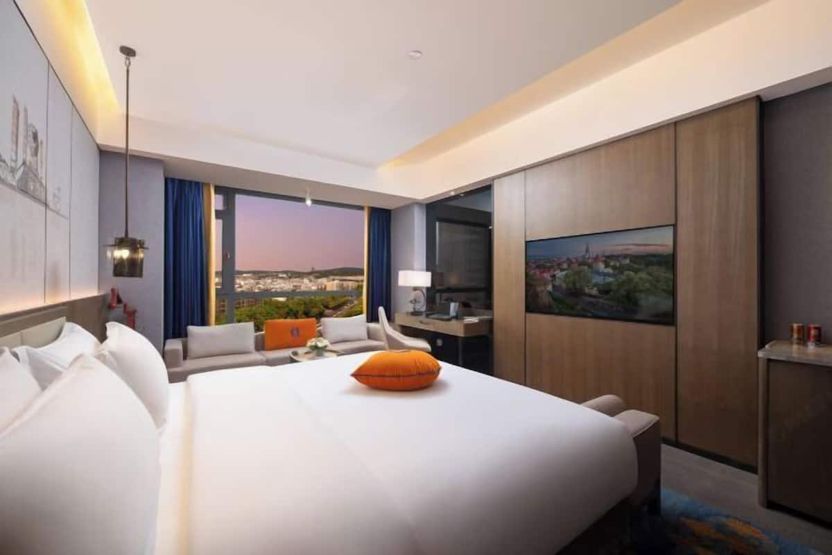 Une chambre d’hôtel avec un grand lit, un bureau, une chaise, une télévision et une vue sur le paysage urbain.