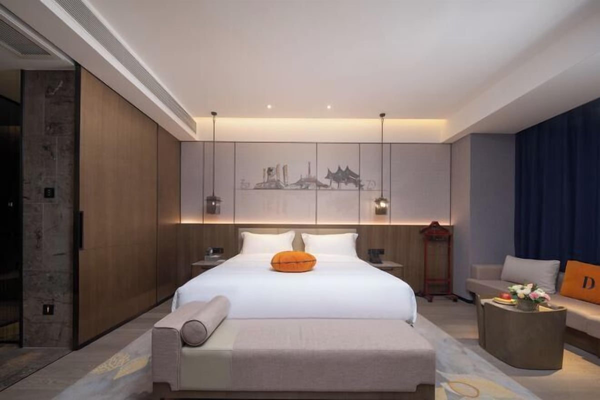 Una habitación de hotel moderna con una cama grande, una mesita de noche y vistas a la ciudad.