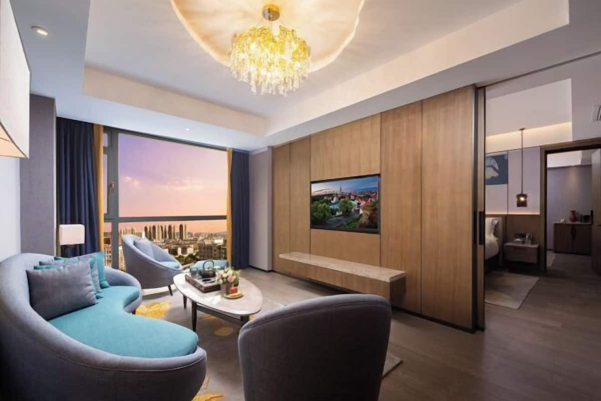 Un salon moderne comprenant un canapé, des fauteuils, une table basse, un téléviseur et une grande fenêtre donnant sur la ville.