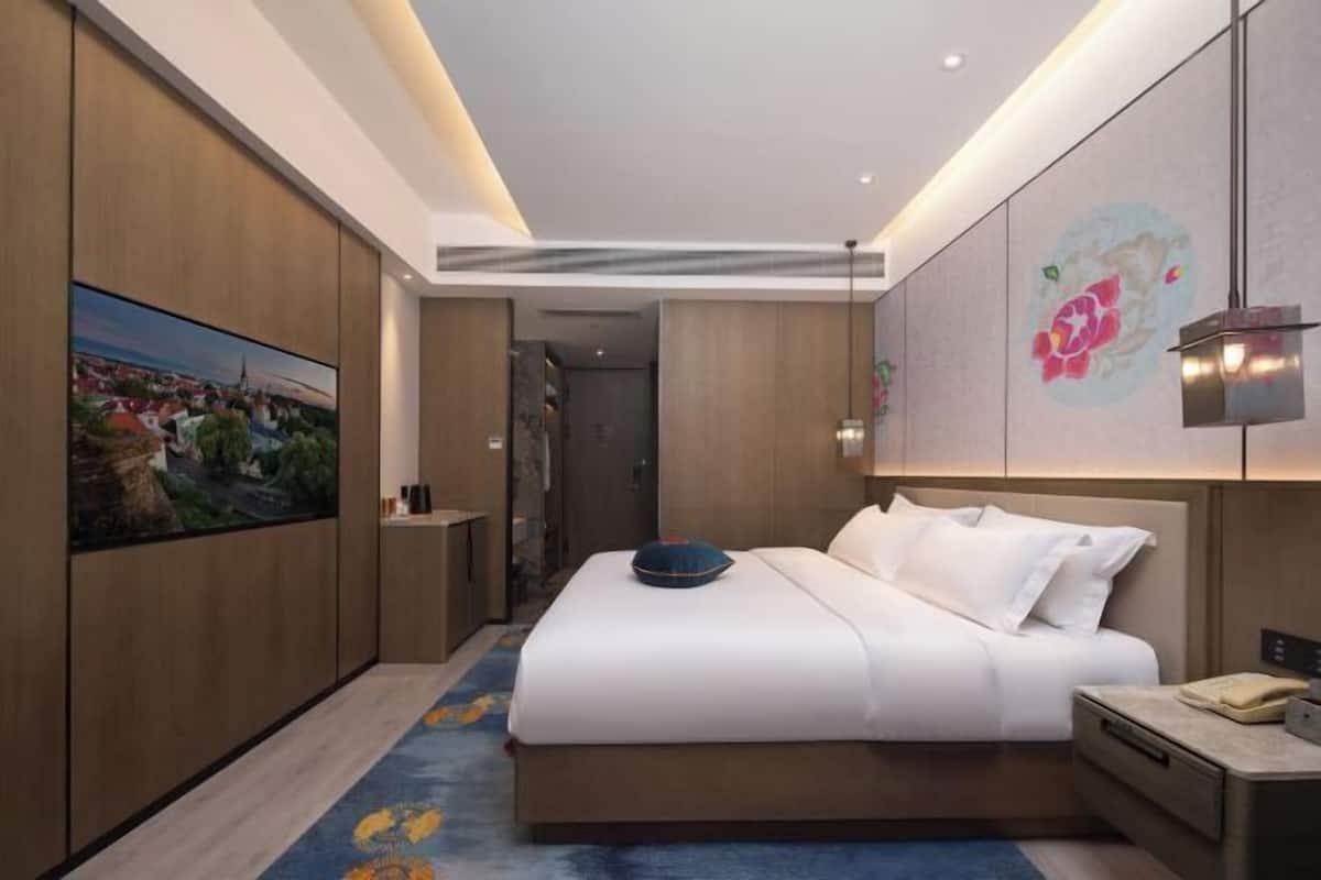 Une chambre d’hôtel moderne dotée d’un grand lit, d’une table de chevet, d’un téléviseur fixé au mur et d’un élément décoratif mural.