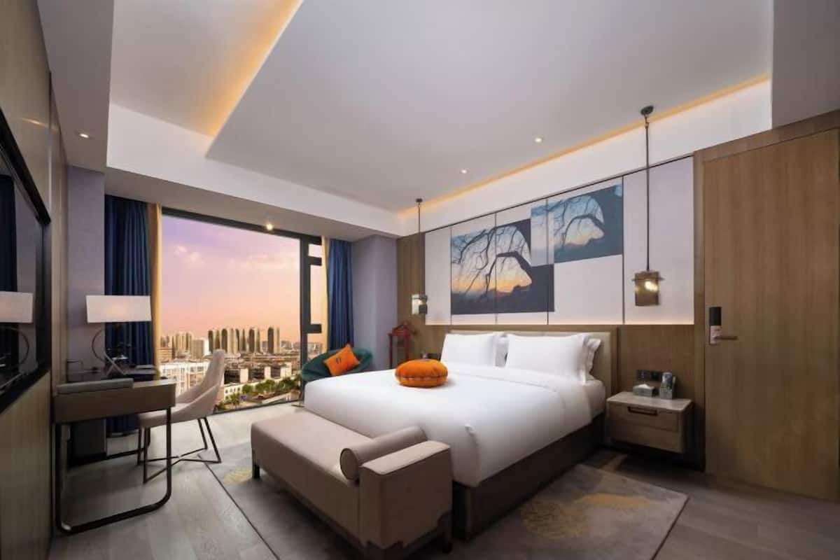Une chambre d’hôtel moderne, dotée d’un grand lit, d’un bureau, d’une chaise et offrant une vue sur le paysage urbain.