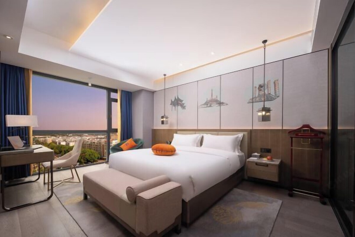 Una habitación de hotel moderna con una cama grande, un escritorio, una silla y vistas a la ciudad.