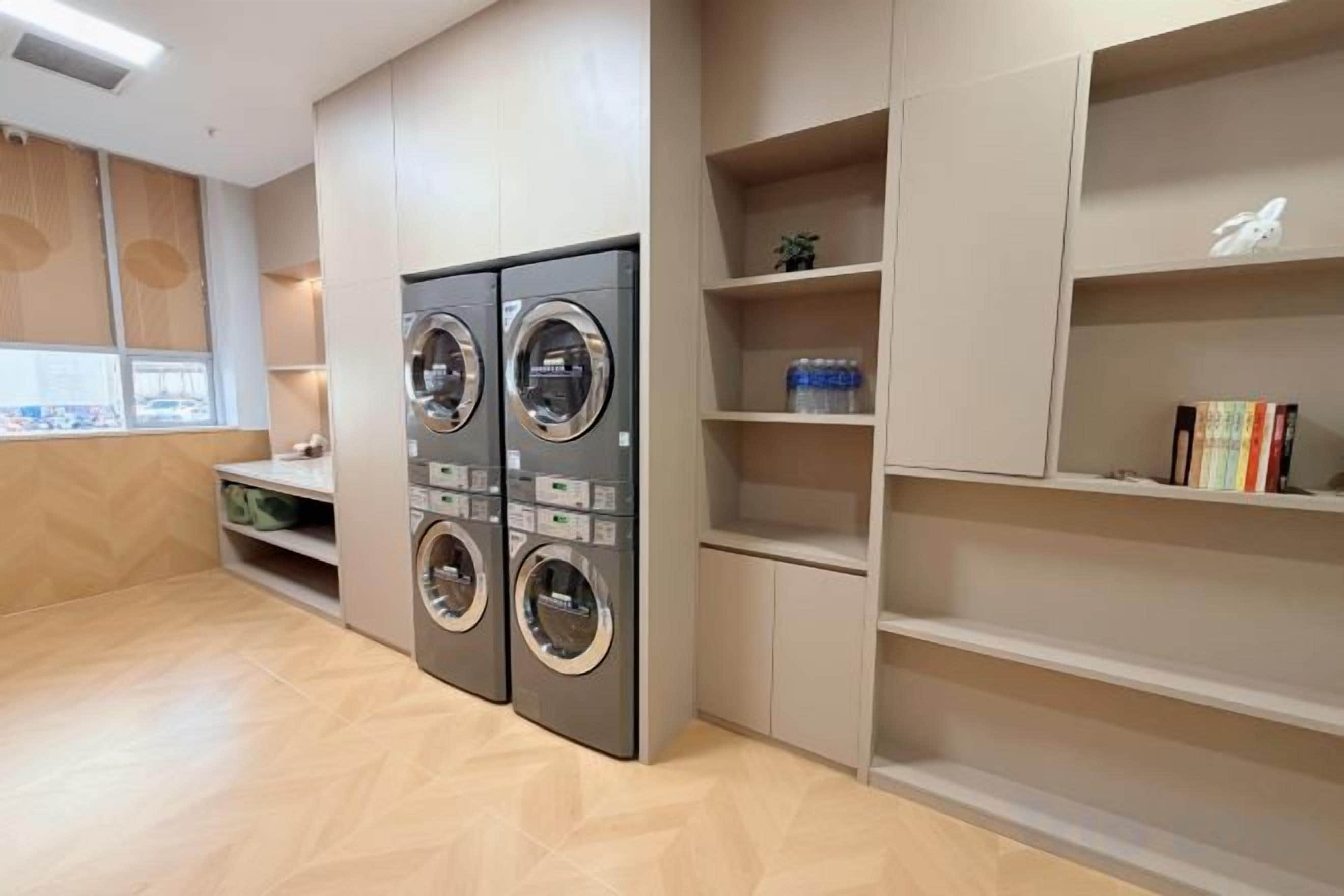 A laundry room with two wall-mounted washing machines, a small seating area, and built-in shelving with books and decorative items.