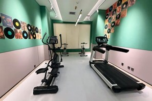 Une salle de sport équipée d’appareils de cardio, d’un tapis de course et d’éléments décoratifs muraux.