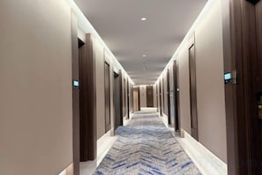 Un pasillo de hotel con puertas a ambos lados, una alfombra estampada y un diseño moderno en el techo.
