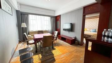 Habitación de hotel con una mesa de comedor, sillas, televisor, sofá, piso de madera y un ventanal grande.