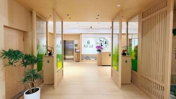 A hallway with a reception desk, potted plants, and a view into the reception area.
