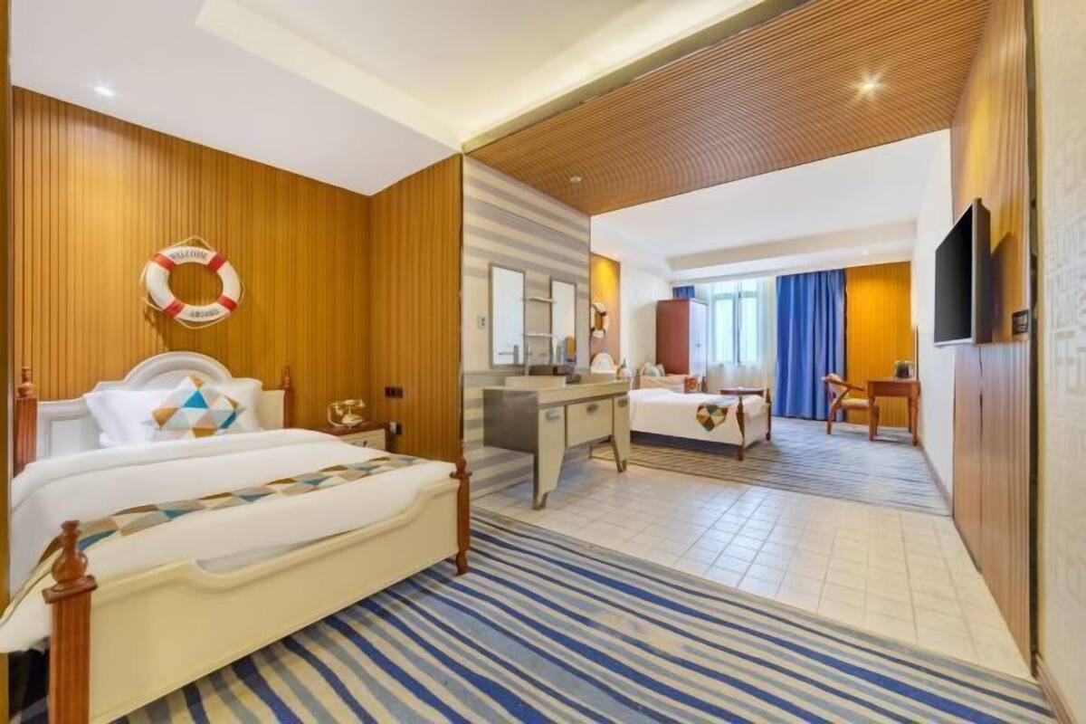 A hotel room with a bed, a desk, a mirror, a dresser, and a television.