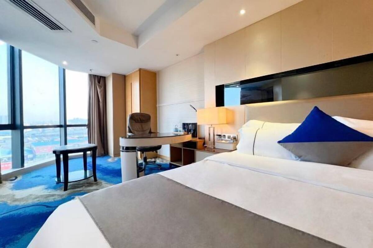A hotel room with a large bed, a desk, a chair, a TV, and a view of the city.